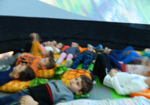 Dzieci w pozycji leżącej oglądają prezentację